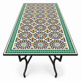 Large rectangular Moroccan zellige mosaic dining table with rich fish-scale tile pattern in olive green warm gold and moss with deep bronze-green border on matte black forged iron Y-fork leg base