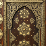 Close-up of arched cedar door panel with gold-tone geometric medallions and floral metal inlay