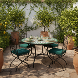 Emerald green zellige mosaic dining table on a verdant garden terrace with lemon trees green cushioned chairs and stone floor