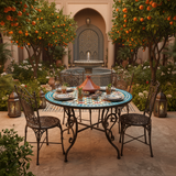 Multicolor zellige mosaic dining table with coral gold teal star pattern in a Moroccan riad courtyard garden with orange trees lanterns tagine dishes and ornate iron chairs